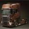 Nákladné vozidlo Scania v tmavohnedom odtieni s nápisom 'Black Amber', dekoratívnym plameňovým vzorom na karosérii a tmavým pozadím.