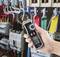 Jedna ruka drží digitálny multimeter s prúdovými kliešťami pred otvorenou rozvodnou skriňou s farebnými káblami a poistkami.