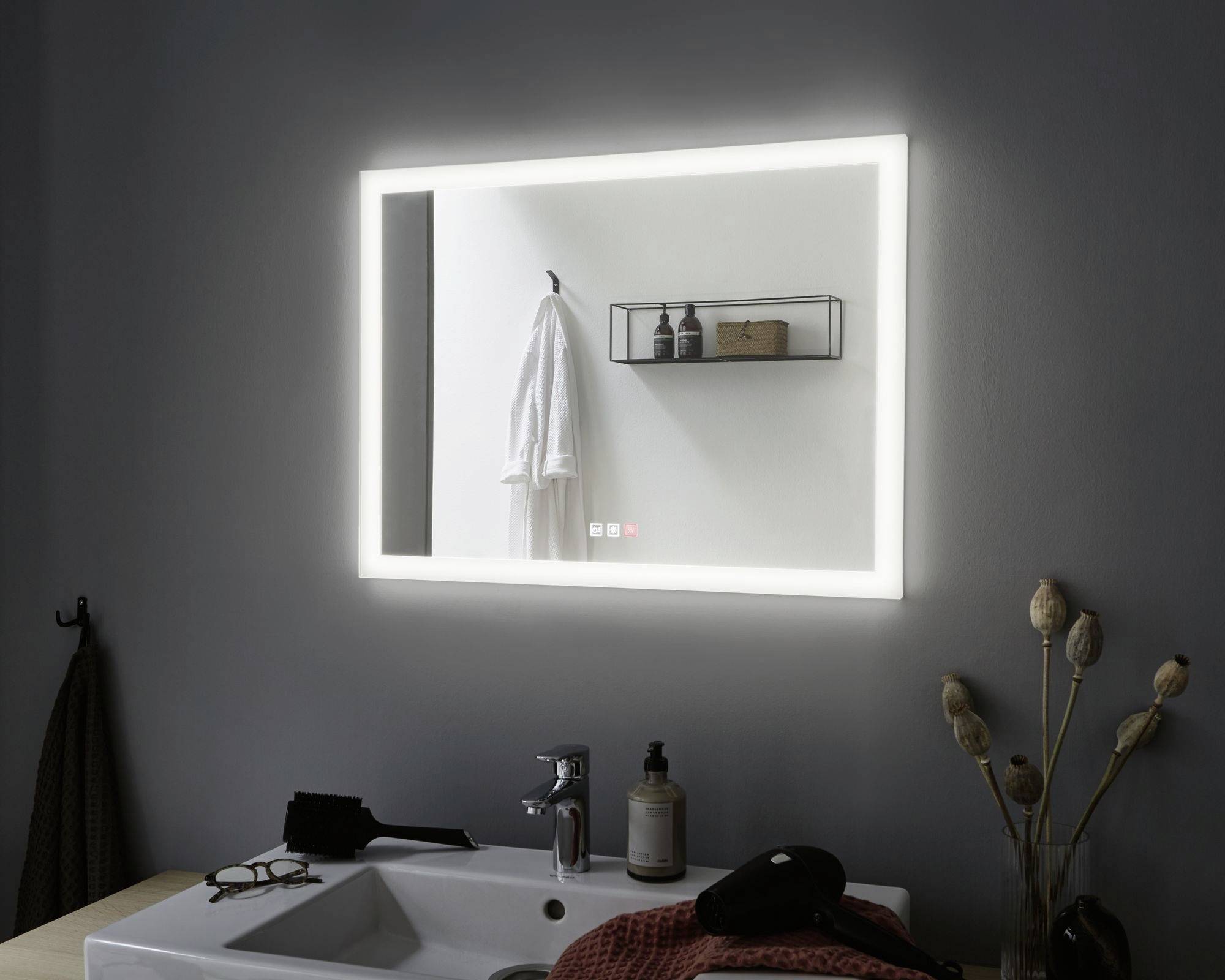 Osvetlené zrkadlo nad umývadlom zobrazuje reflexie uterákov a kúpeľňových doplnkov na poličke na stene.