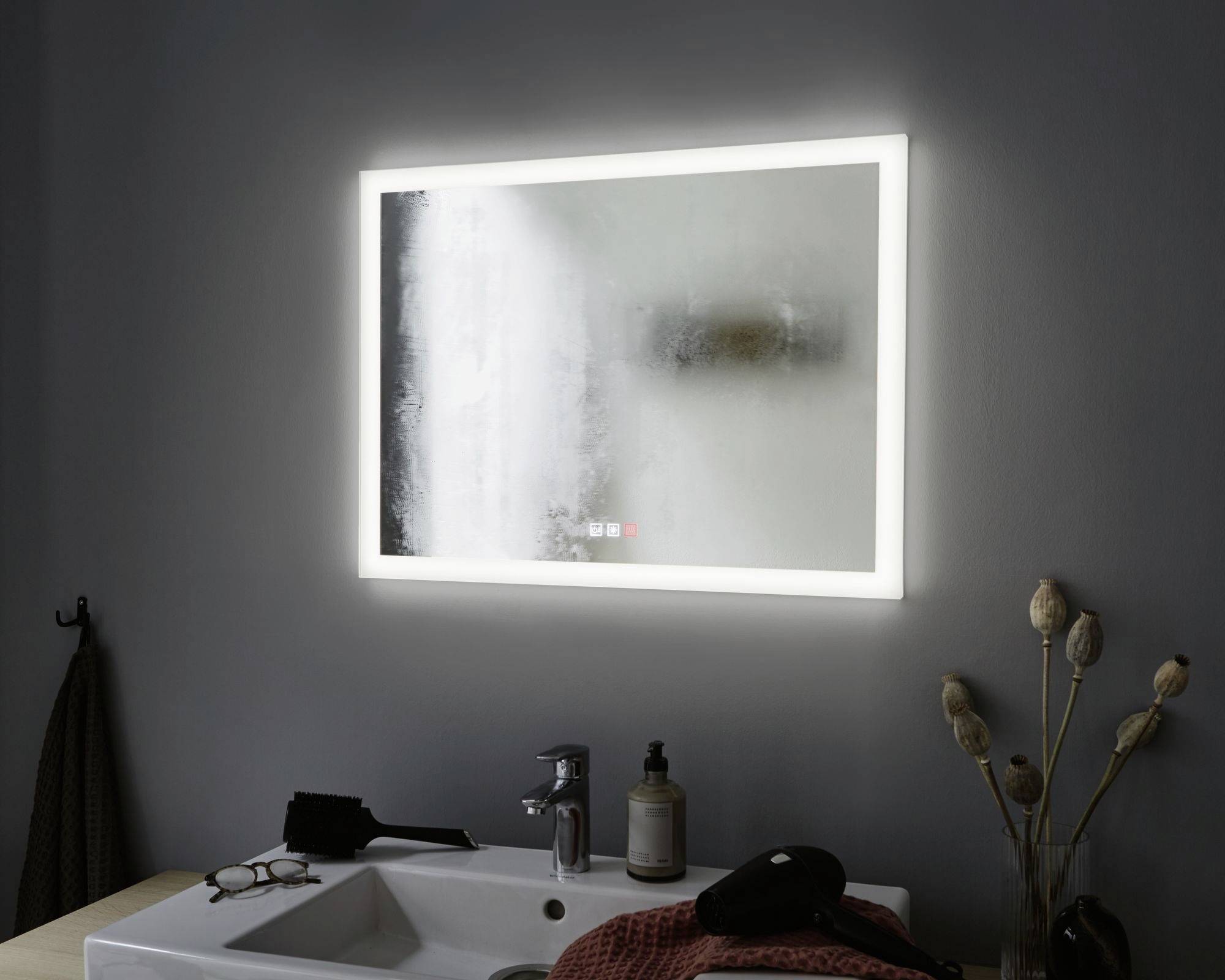Zarosené kúpeľňové zrkadlo so svetlým LED rámom nad umývadlom, na ktorom ležia kefa, okuliare a uterák.