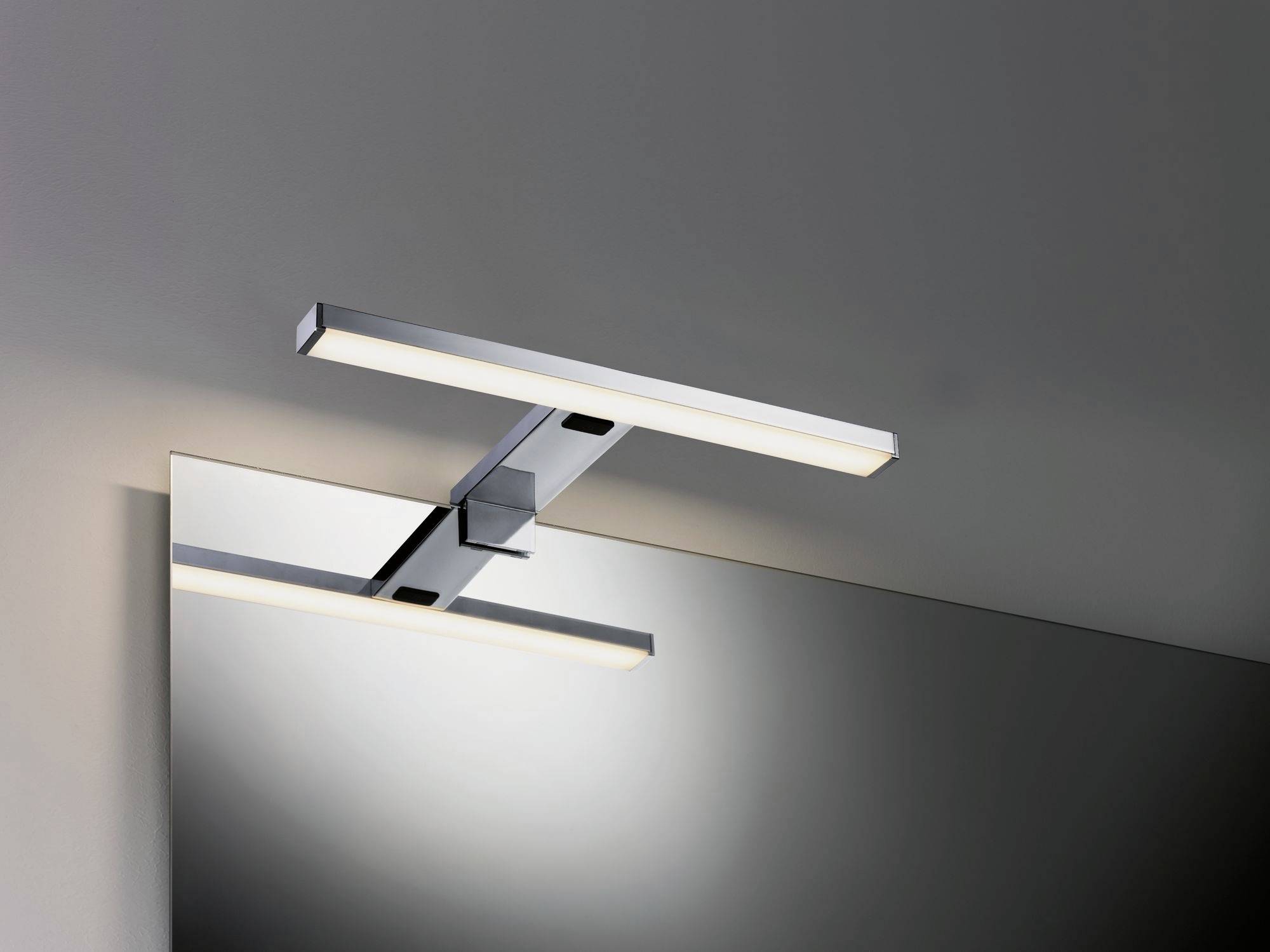 Moderná obdĺžniková LED nástenná lampa namontovaná nad zrkadlom na sivej stene, osvetľuje priestor pod ňou.