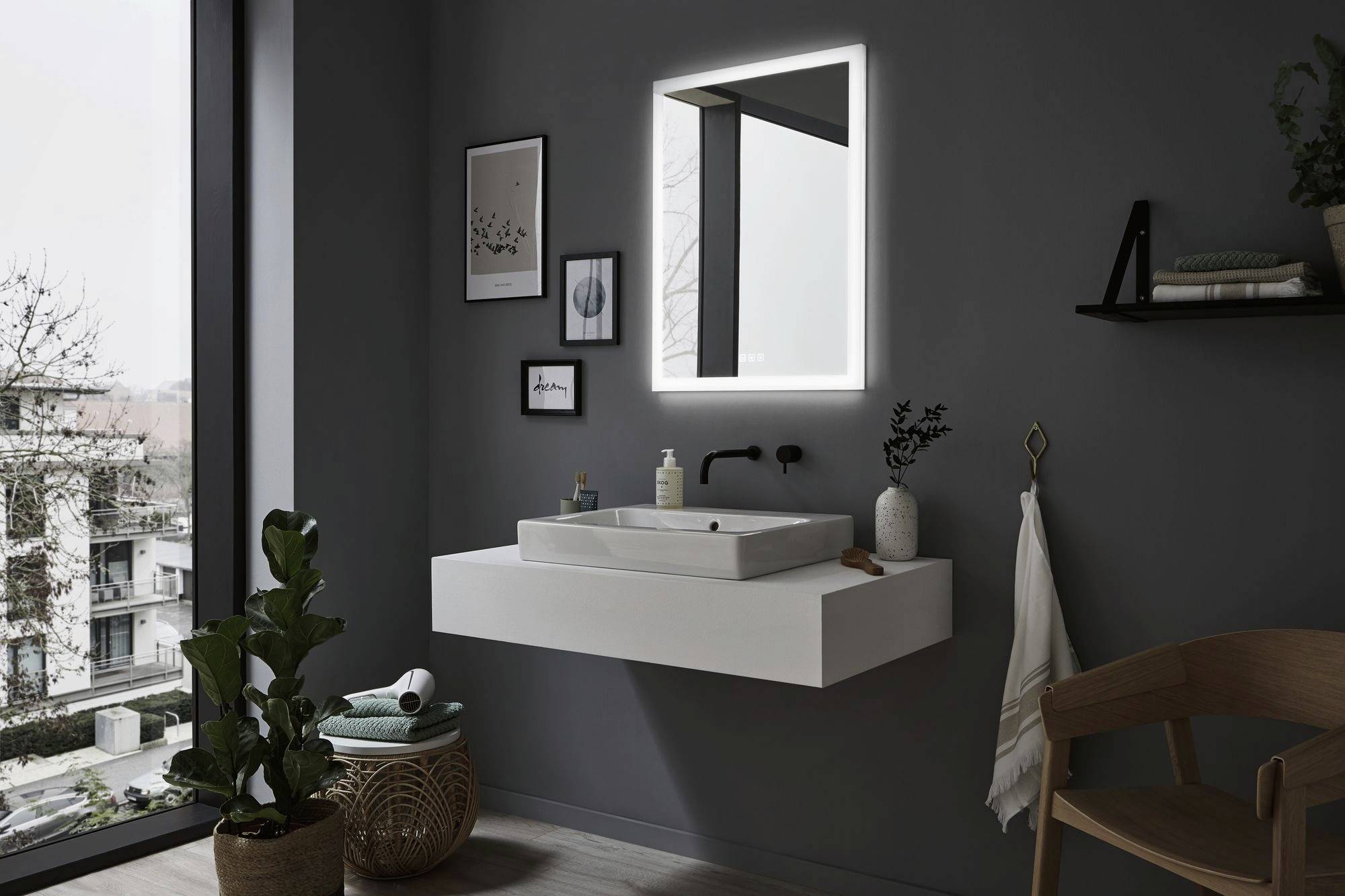 Moderná kúpeľňa s voľne umiestneným umývadlom, osvetleným zrkadlom a tmavými stenami. Rastliny a dekorácie dopĺňajú priestor.