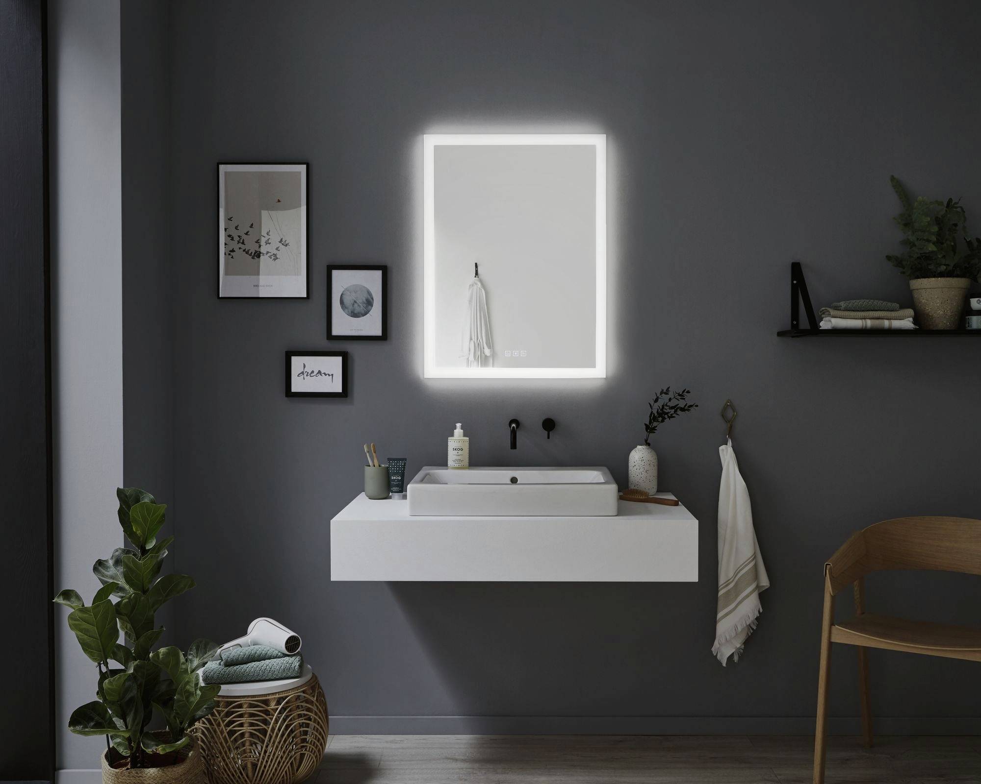 Moderný kúpeľňový priestor s osvetleným zrkadlom, bielym umývadlom na stenových konzolách, rastlinami a dekoráciami na tmavej stene.