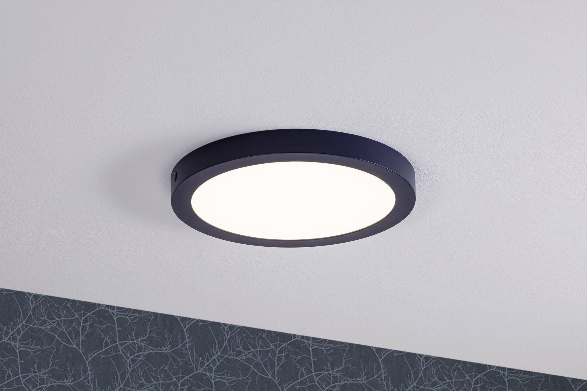 Okrúhle LED stropné svietidlo s čiernym lemom, namontované na bielom strope. Rovnomerne osvetľuje priestor.