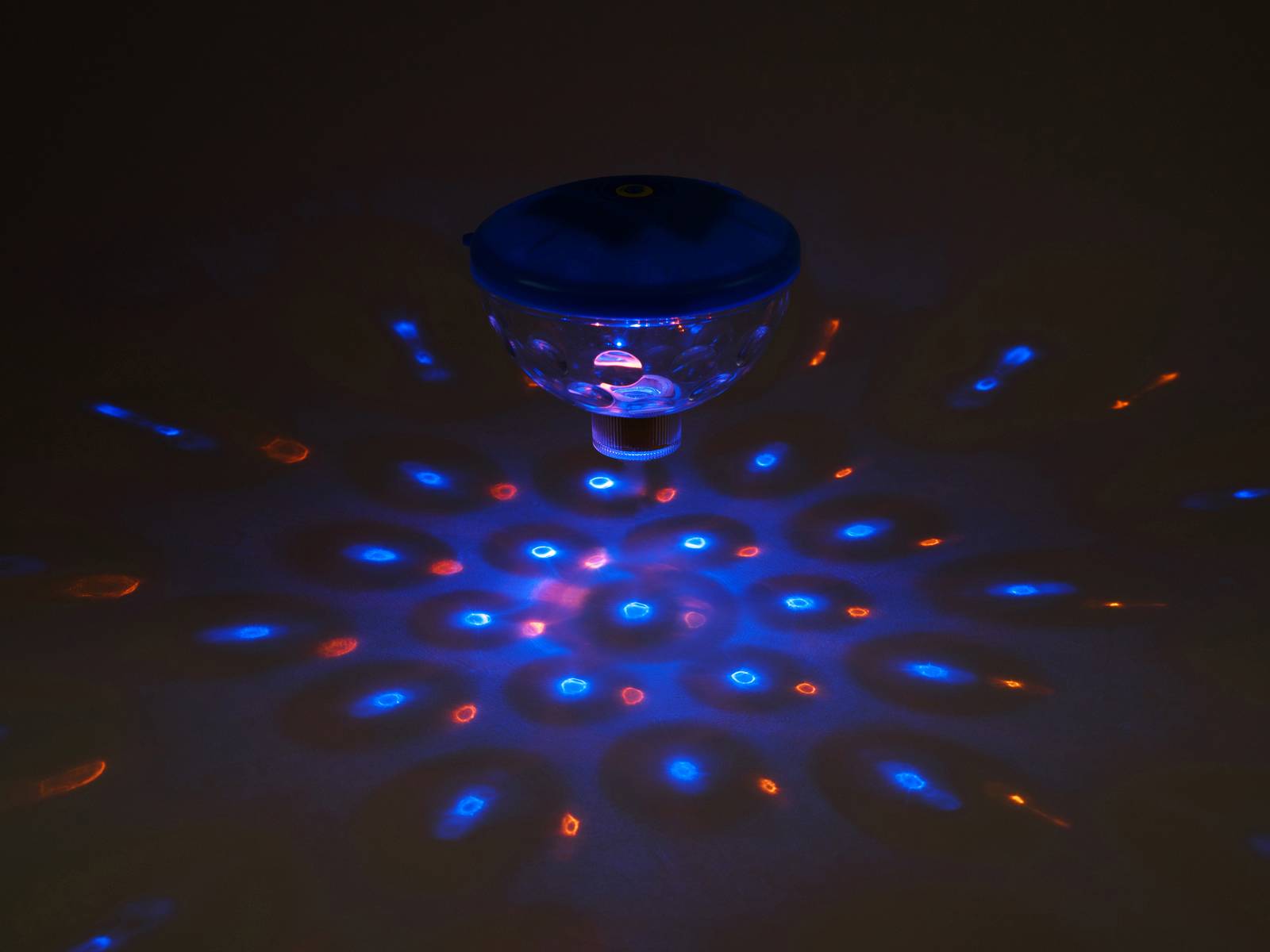 Sklenený predmet sa otáča a premieta pestré, modré a červené svetelné vzory na tmavý povrch, ktorý pripomína kaleidoskop.