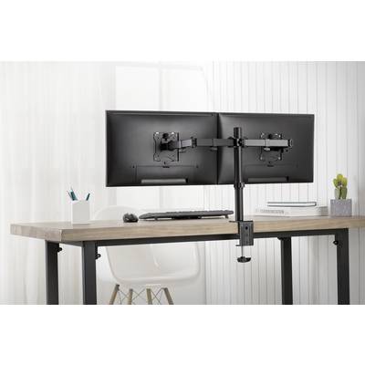 Dva monitory na písacom stole s držiakom pre duálny monitor; v pozadí okná, vedľa stoličky a dekorácie.