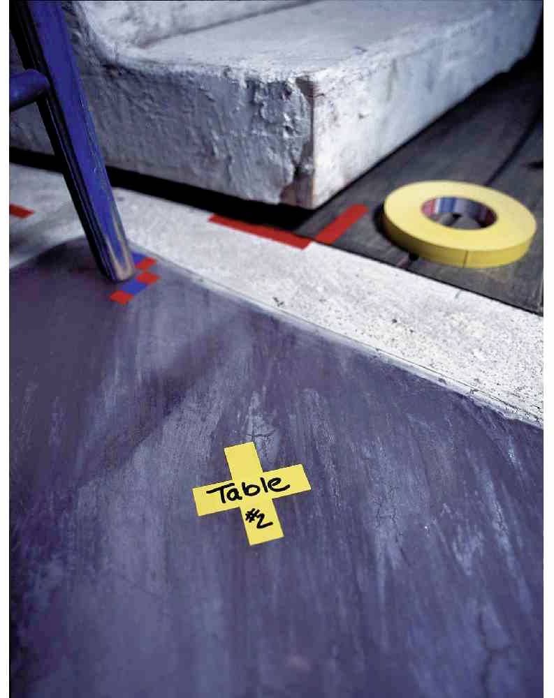 Podlahové označenie žltou lepiacou páskou vo forme kríža, na ktorom je napísané 'Stôl č. 2'. V pozadí je schodík a žltá lepiaca páska.
