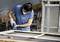 Osoba opracúva staré okno brúskou v dielni. Má na sebe ochranné okuliare a rukavice.