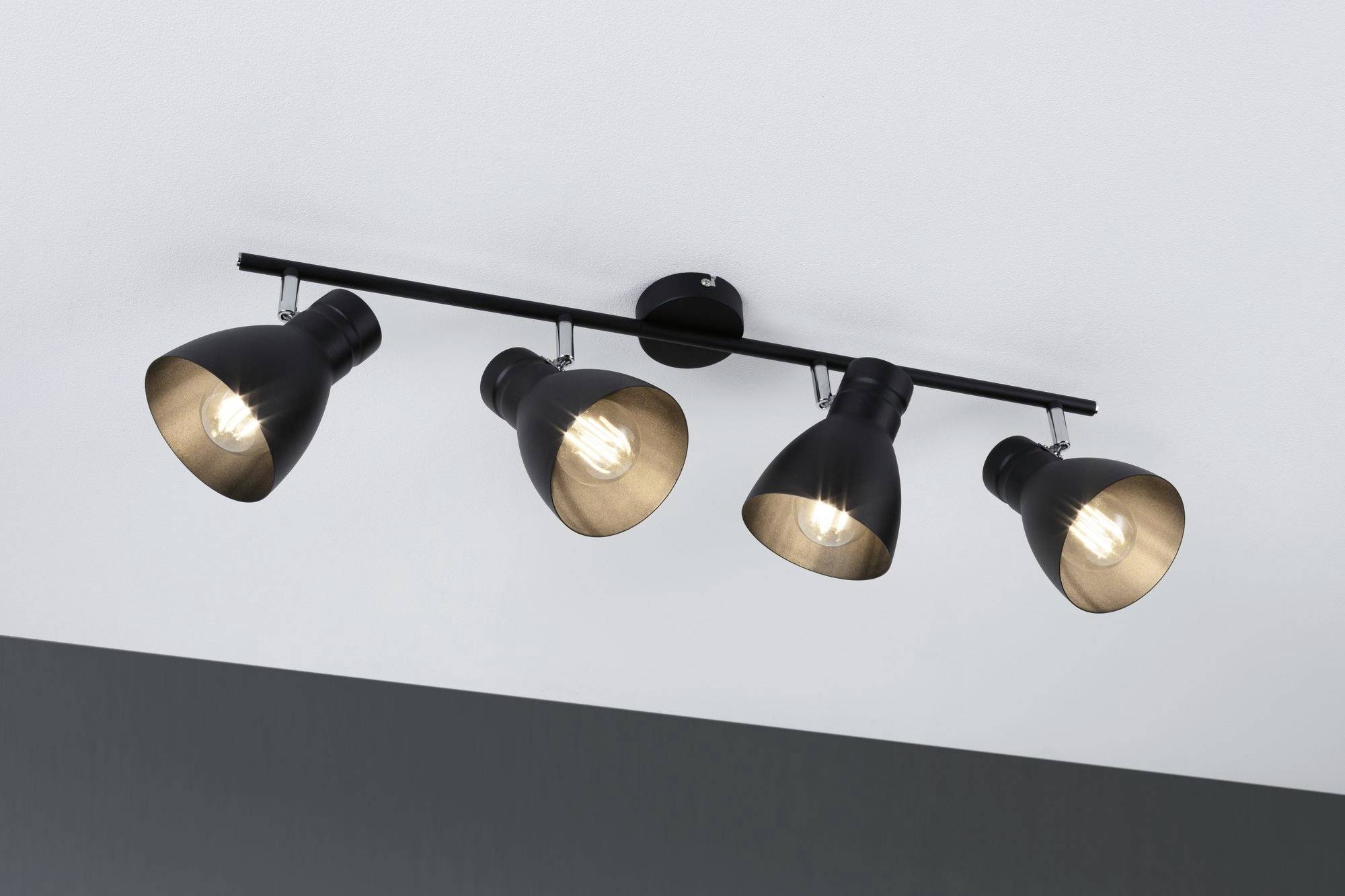Štyri čierne stropné reflektory, každý s jednou žiarovkou, sú namontované na lište a upevnené na bielom strope.