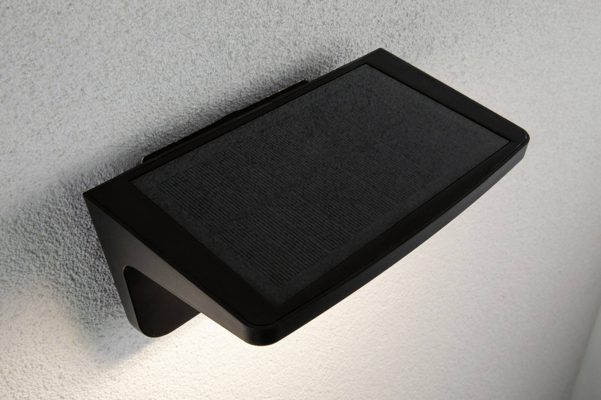 Vonkajšie nástenné svietidlo so solárnym panelom, namontované na bielej stene, pre energeticky úsporné osvetlenie.