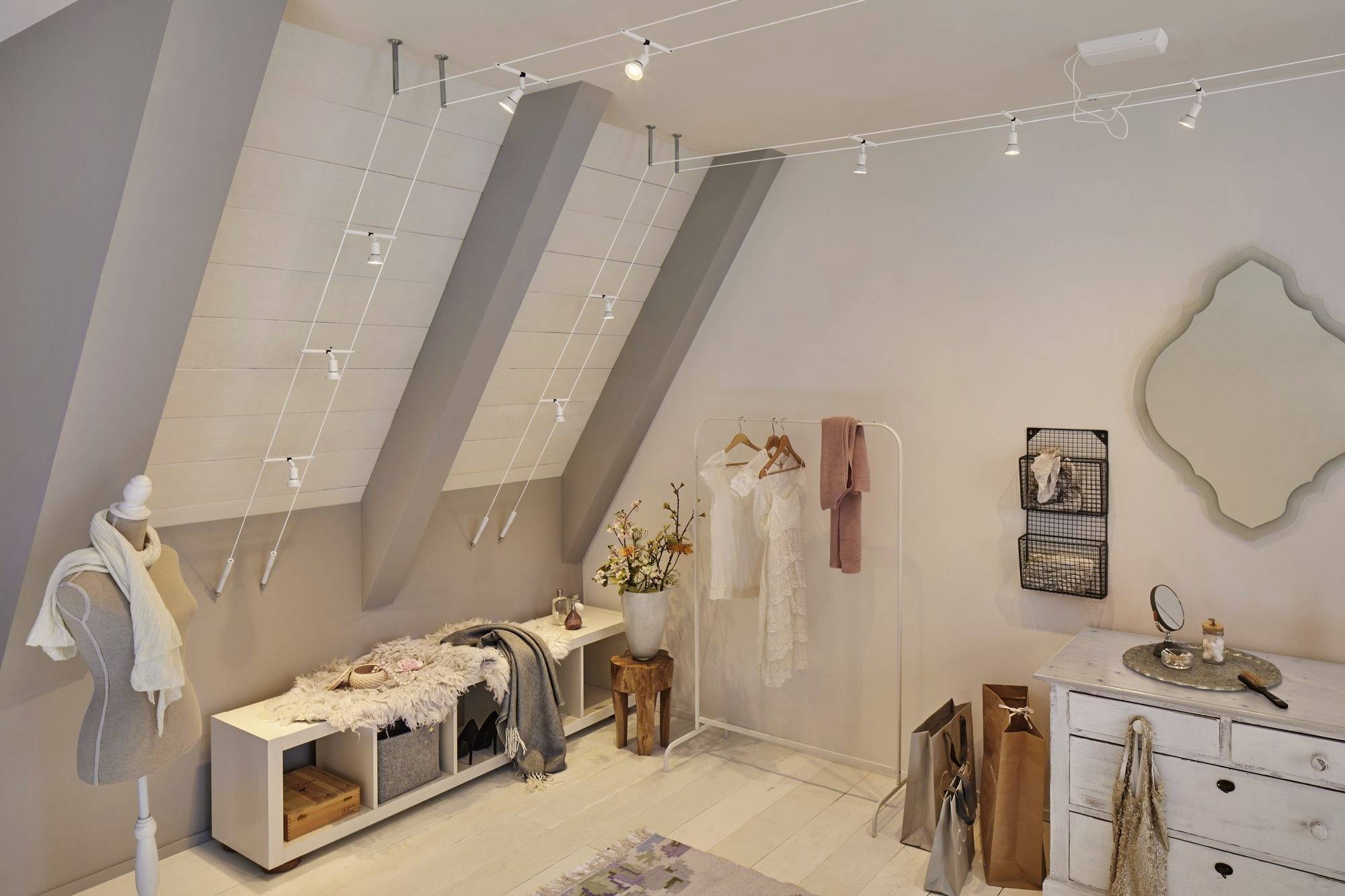 Štýlovo zariadená miestnosť so šikmým stropom. Vešiak na šaty s visiacim oblečením, zrkadlom, dekoráciami a sedacími priestormi.