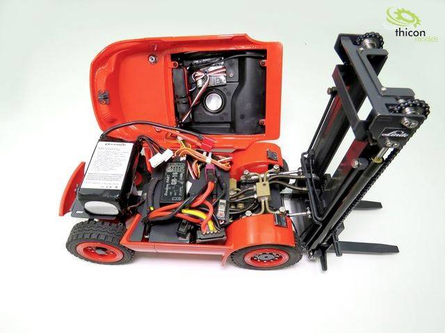 Malý červený modelový vysokozdvižný vozík s otvoreným krytom odhaľuje internú elektroniku a káble, v pozadí je logo.