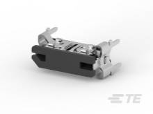 Malý, tmavý konektor s kovovými svorkami na oboch stranách, vhodný pre pripojenie elektronických zariadení.
