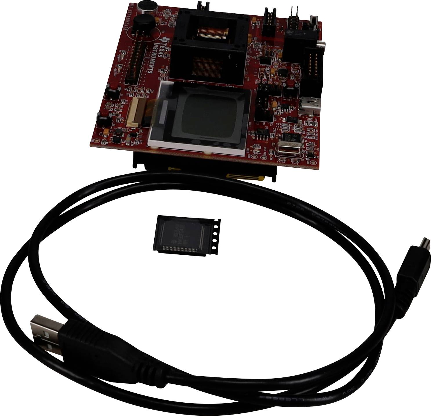 Červená doska plošných spojov s rôznymi čiernymi komponentmi a malou obrazovkou, vedľa USB kábla a mikroprocesorovej čipky, na bielom pozadí.