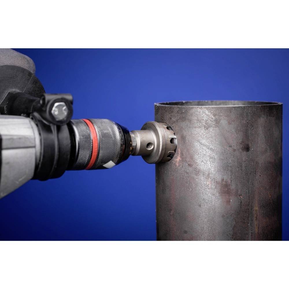 Vŕtačka opracúva hrubú kovovú rúru pred modrým pozadím, zobrazuje presnú kovovýrobu alebo remeselnú prácu.