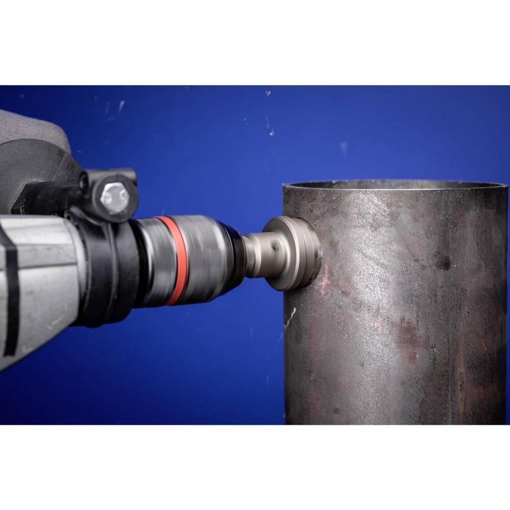 Stroj vŕta veľkú dieru do kovového potrubia. Detailný pohľad na vrtáka a potrubie pred modrým pozadím.