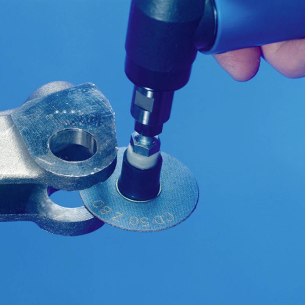 Jedna ruka drží nástroj, ktorý opracováva kovovitý povrch s gravírovaným označením 'CD50Z8'.