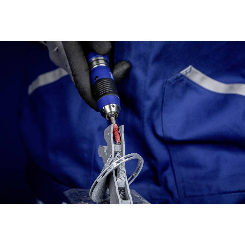 Osoba v modrom pracovnom oblečení brúsi kovový kus ručným náradím. Detailný záber bez viditeľnej tváre.