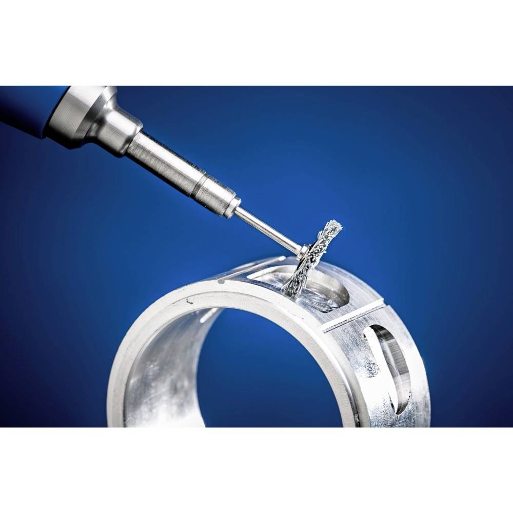 Vŕtačka opracúva kovový krúžok na modrom pozadí. Kovové triesky sú viditeľné.