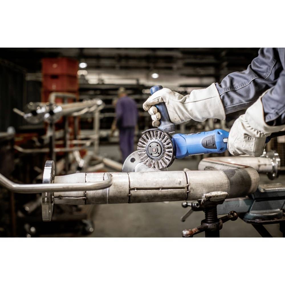 Osoba pracuje v dielni a používa elektrické brúsne zariadenie na opracovanie kovového potrubia.