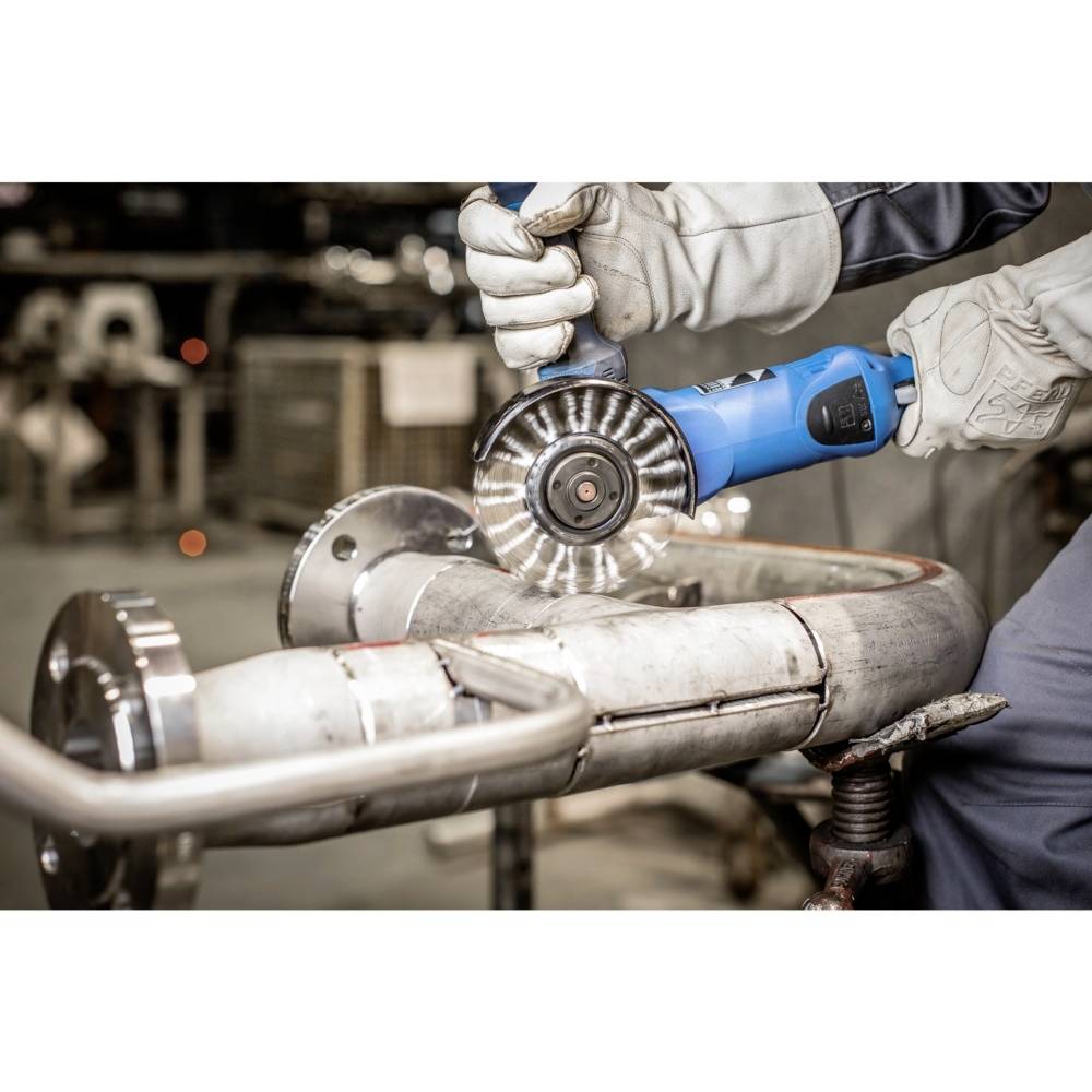 Robotník v rukaviciach používa modrú uhlovú brúsku na rezanie kovových rúr. Prostredie je dielňa.