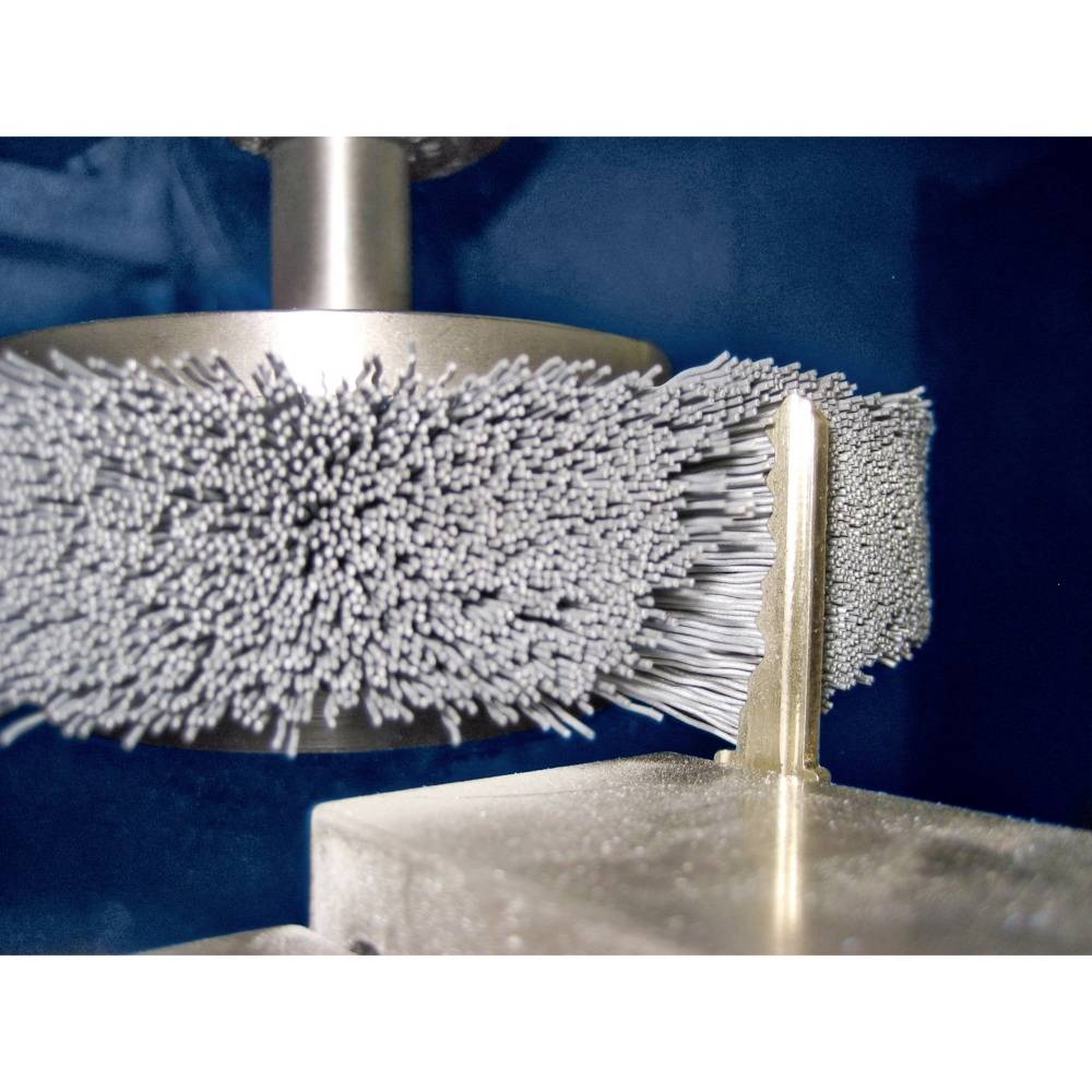 Stroj s rotujúcou kefou opracováva kovový obrobok. Štetiny kefy sa javia v pohybe.