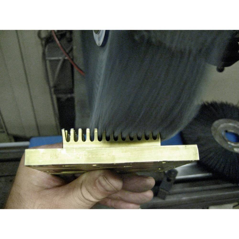 Ruka drží kovový diel so zúbkatým okrajom pred rotujúcim brúsnym kotúčom v dielni.