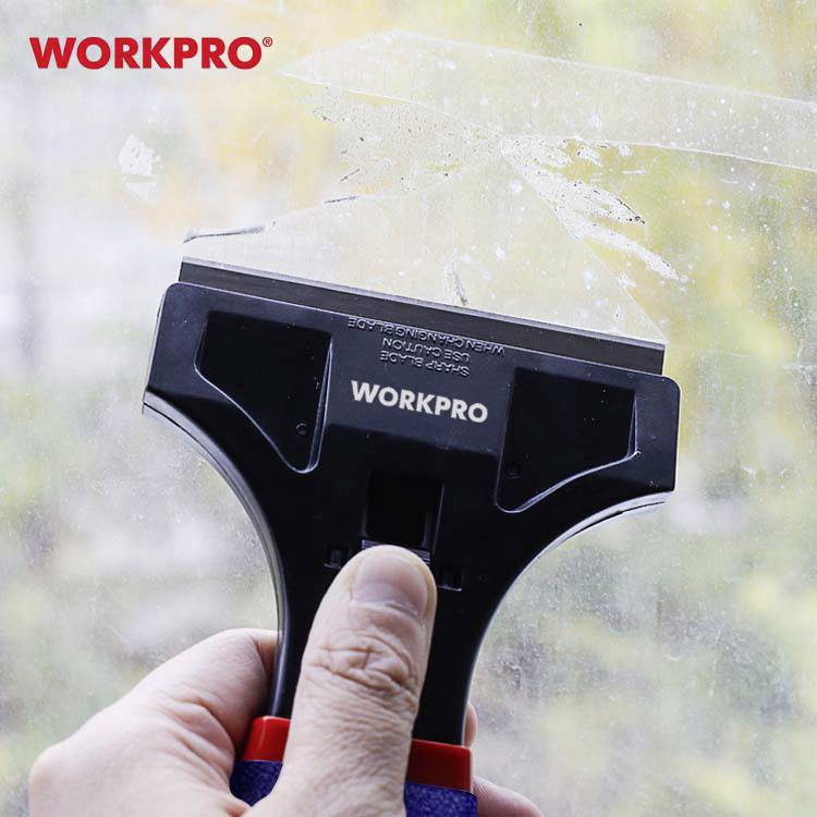 Ruka drží sklenený škrabák WORKPRO a odstraňuje farbu z okna.