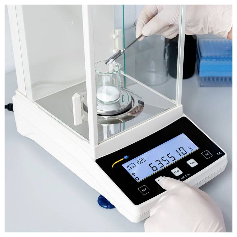 Rukavičkami chránené ruky používajú laboratórnu analytickú váhu na zváženie vzorky v kadičke, pričom digitálny displej zobrazuje 6355,18 g.