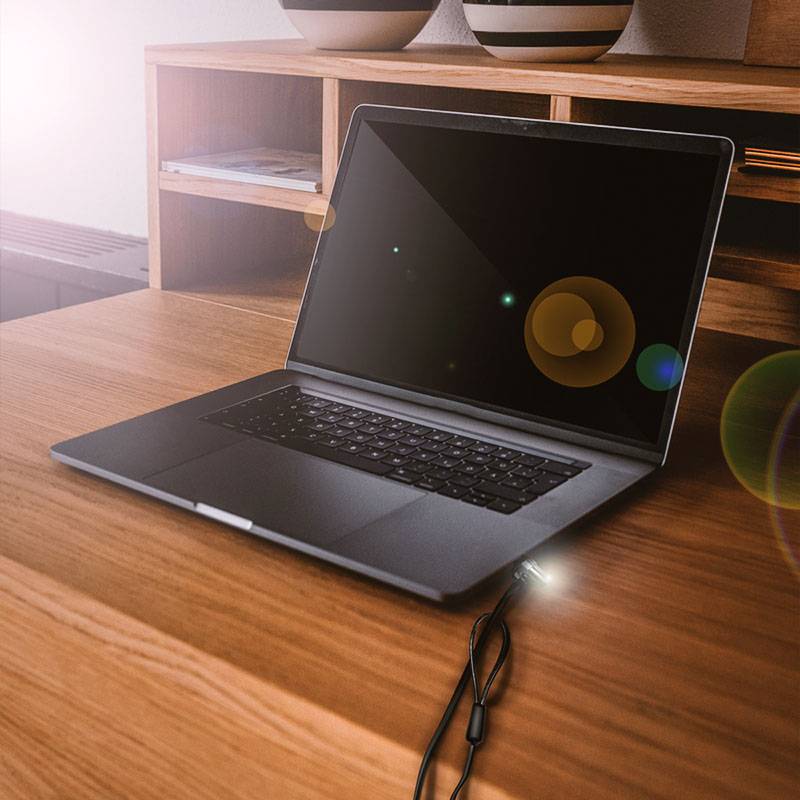 Laptop na drevenej stolnej doske v kancelárii, obrazovka je vypnutá. Kábel je zapojený. V pozadí políc s knihami.