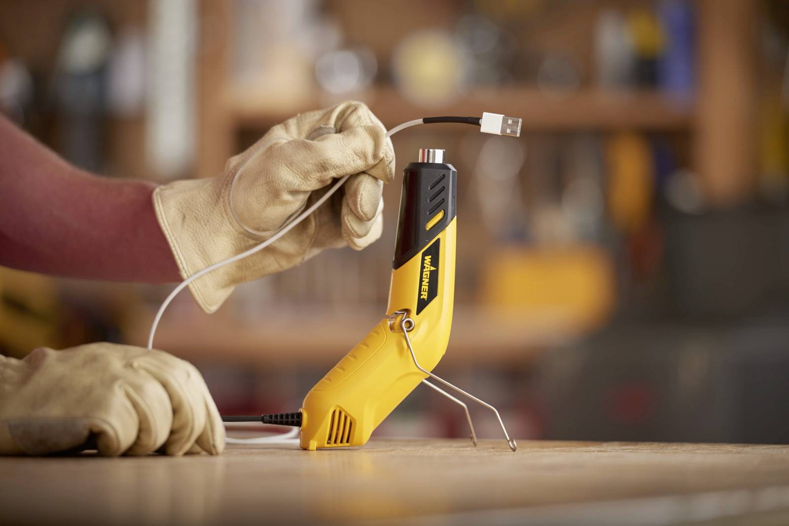 Osoba v pracovných rukaviciach drží USB kábel nad žltým multifunkčným nástrojom v dielni.