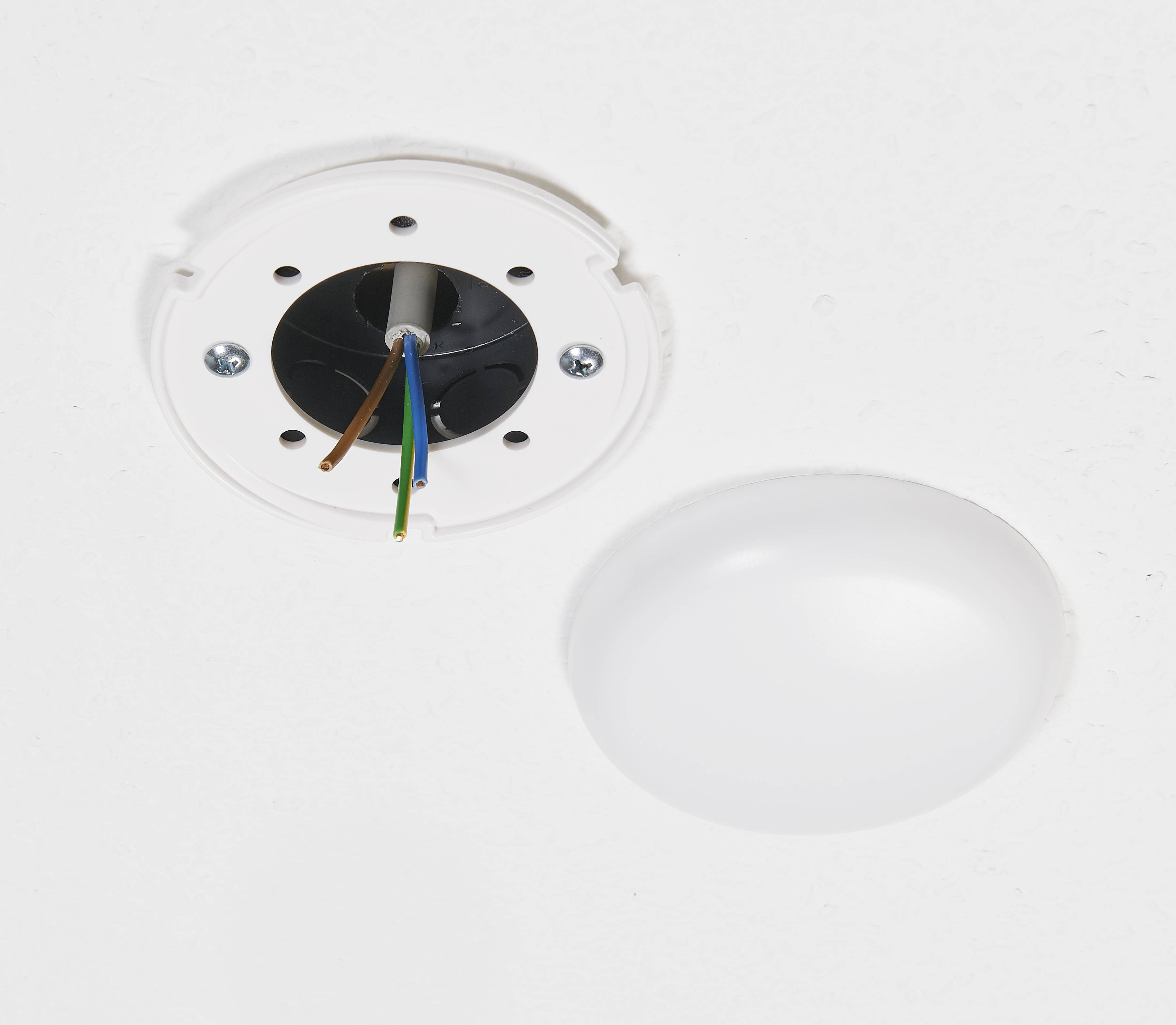 Sňatá stropní lampa odhaluje volně vedené vodiče na stropě, vedle ní leží sejmutý kryt lampy.