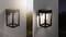 Nástenná lampa v modernom, štvorcovom dizajne, rozsvecujúca sa v súmraku, namontovaná na vonkajšej stene s záhradou v pozadí.