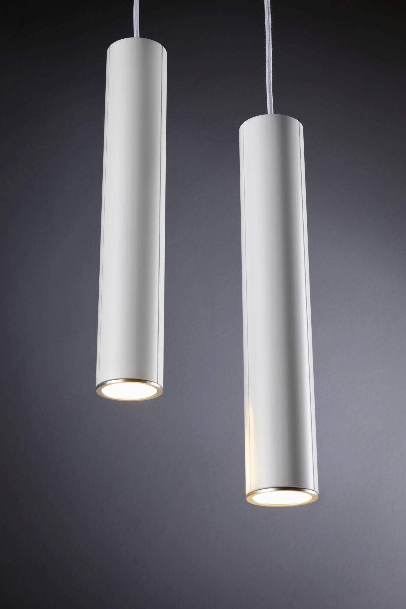 Dva zavesené válcové biele stropné svietidlá svietia na sivom pozadí. Sú moderne a minimalisticky navrhnuté.