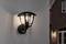 Vonkajšia lampa na stene domu, ktorá je zapnutá v súmraku. V pozadí tehlový dom s osvetleným oknom.