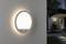 Moderná okrúhla vonkajšia lampa s pohybovým senzorom svieti na stene domu. V pozadí je vstup s osvetlenou cestou.