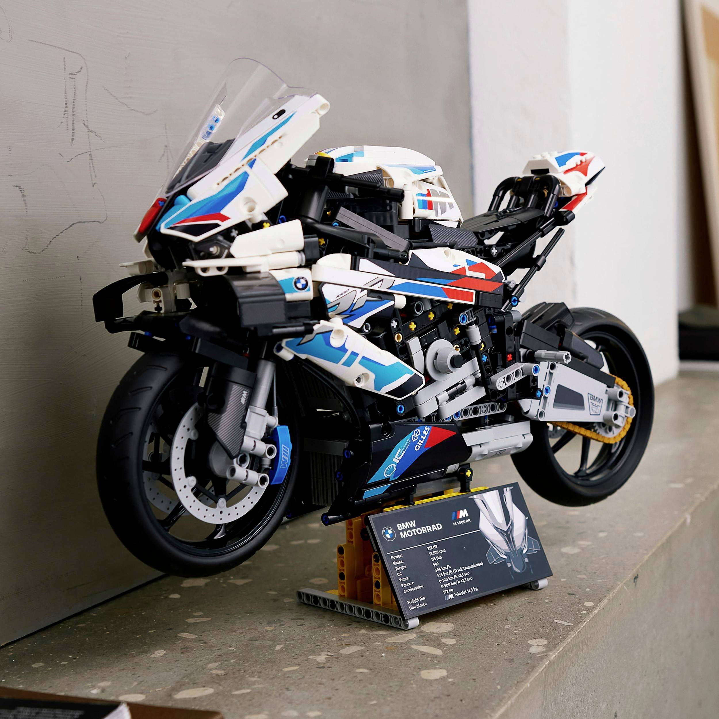 Detailný Lego model motocykla stojí na sivom stole. V popredí je informačná tabuľka so špecifikáciami.