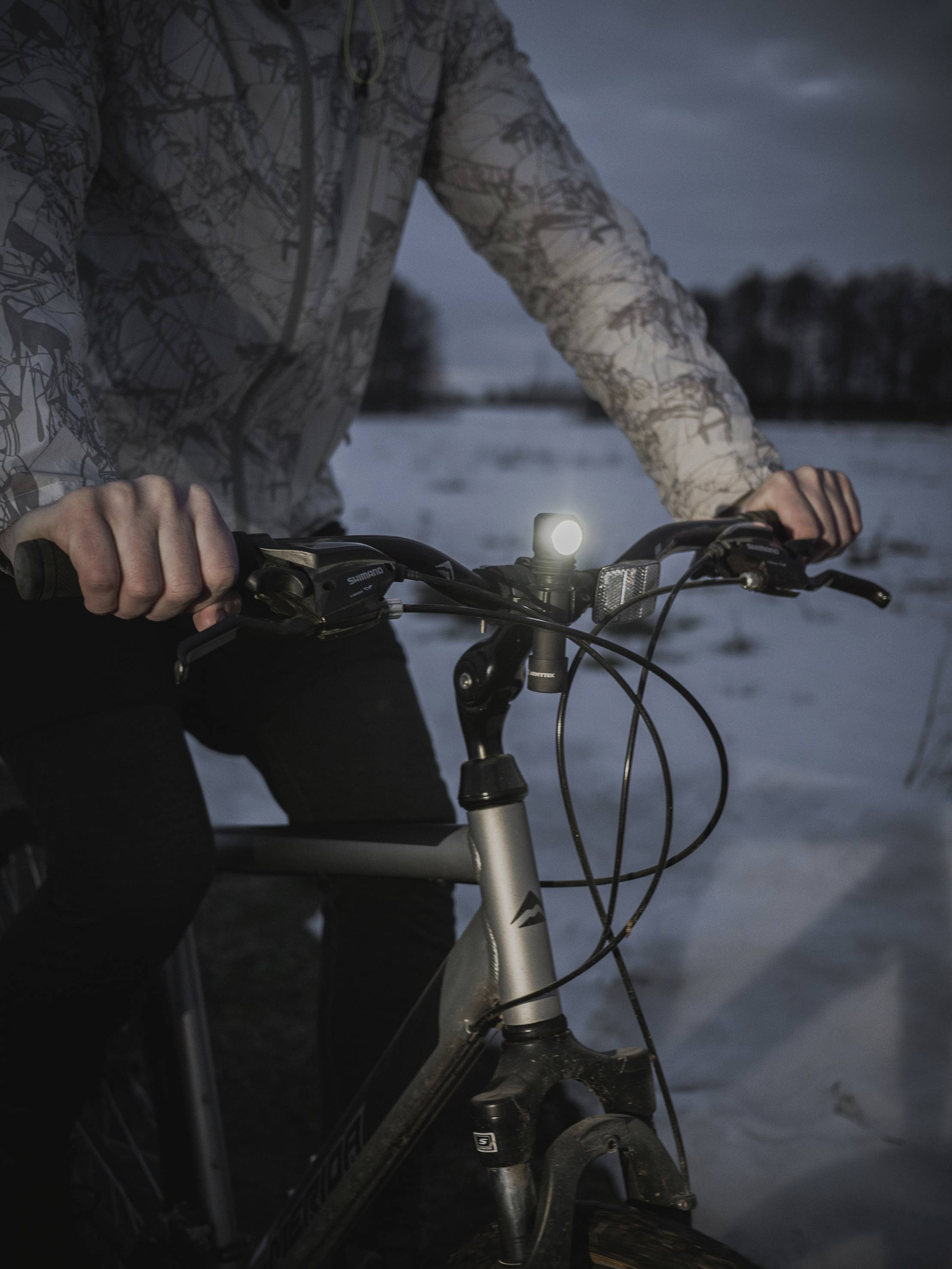 Osoba ide na bicykli so zapnutým svetlom v krajine pokrytej snehom za súmraku.