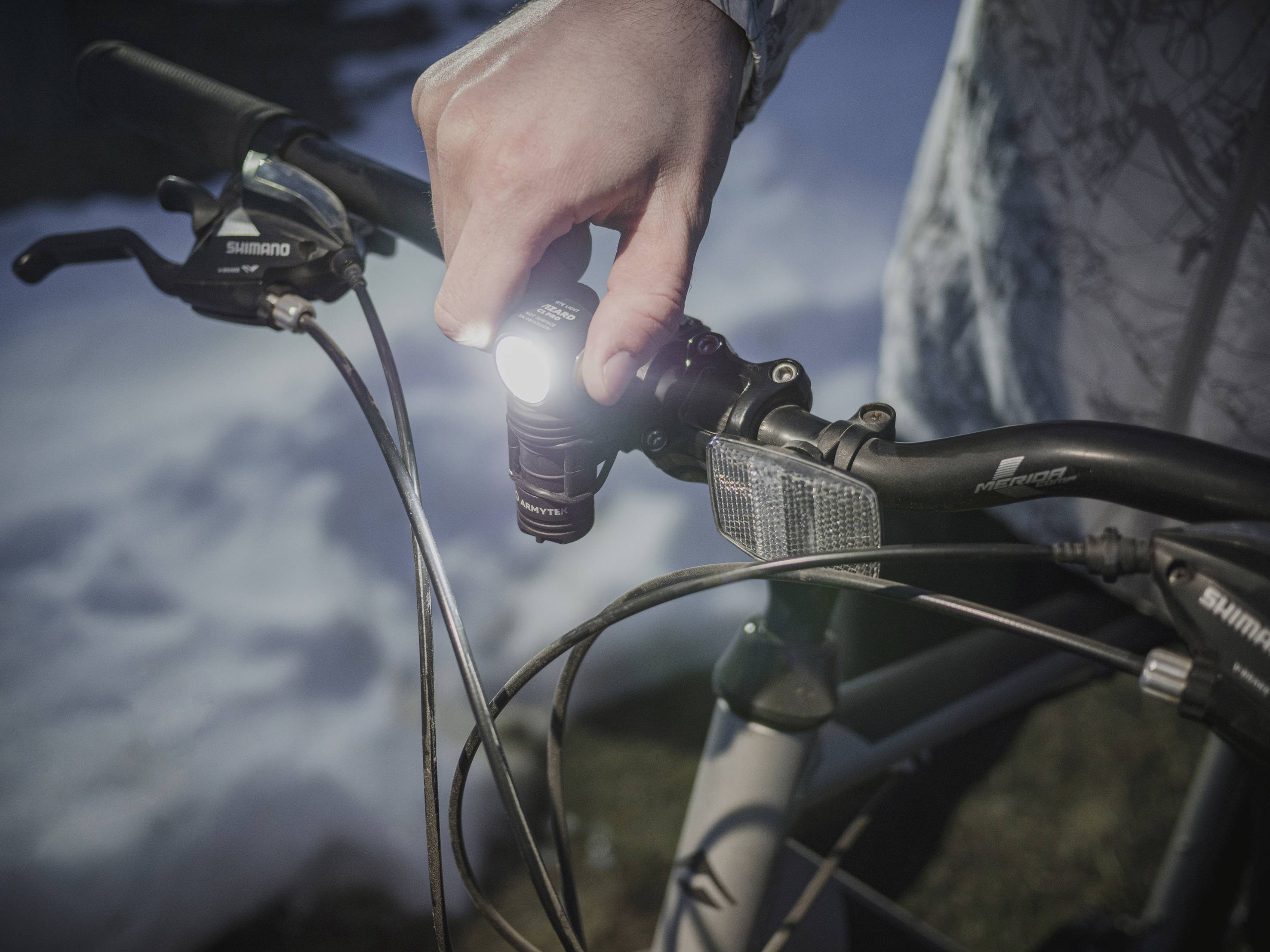 Osoba drží riadidlá bicykla so zapnutým svetlom v tmavom prostredí. V pozadí je zasnežený povrch.