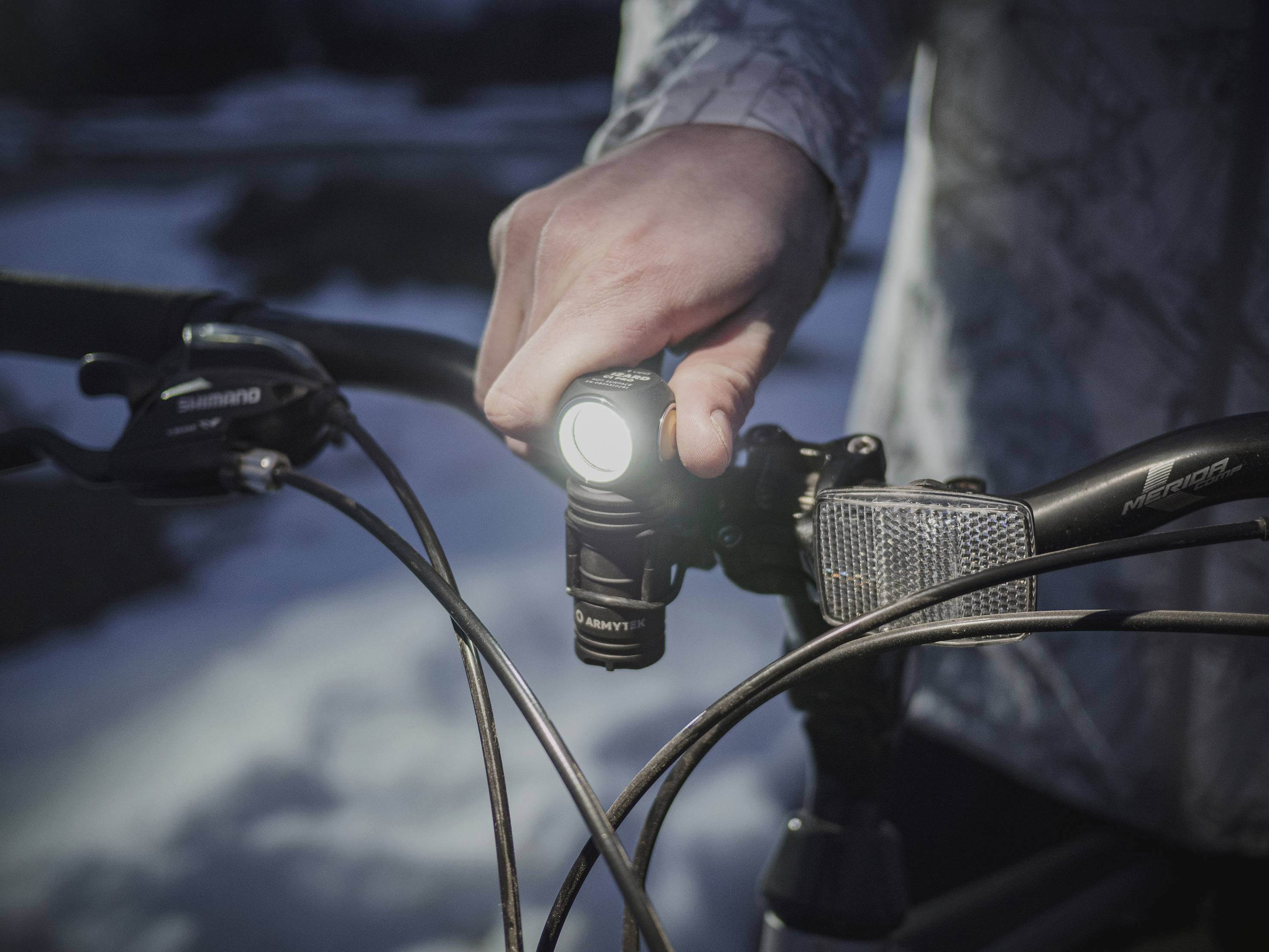 Osoba zapína svetlo na bicykli v tme. Bicykel stojí vonku, obklopený snehom.