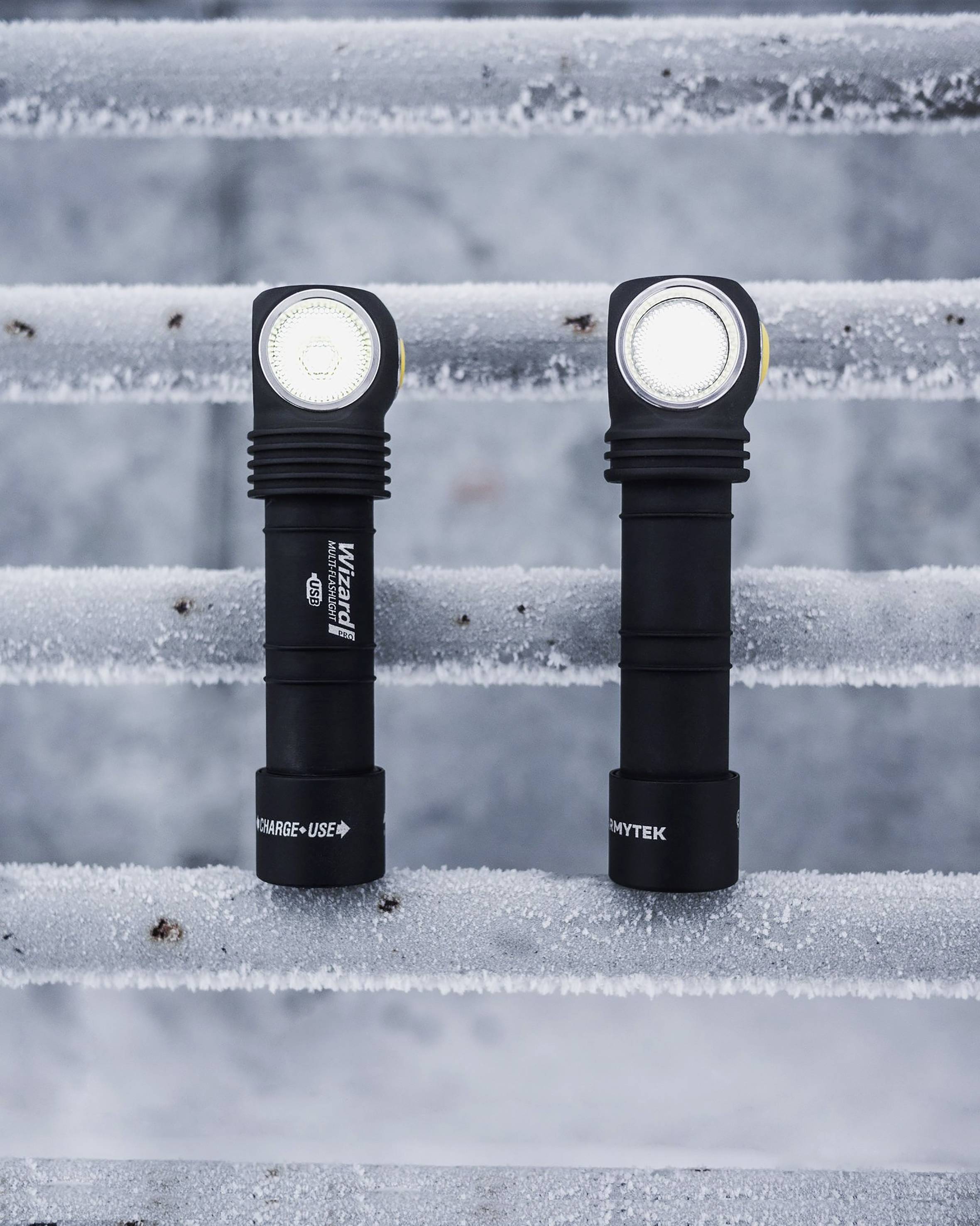 Dve baterky stoja vertikálne na zamrznutých kovovým schodoch. Obe majú svietiace LED lampy a čierne rukoväte.