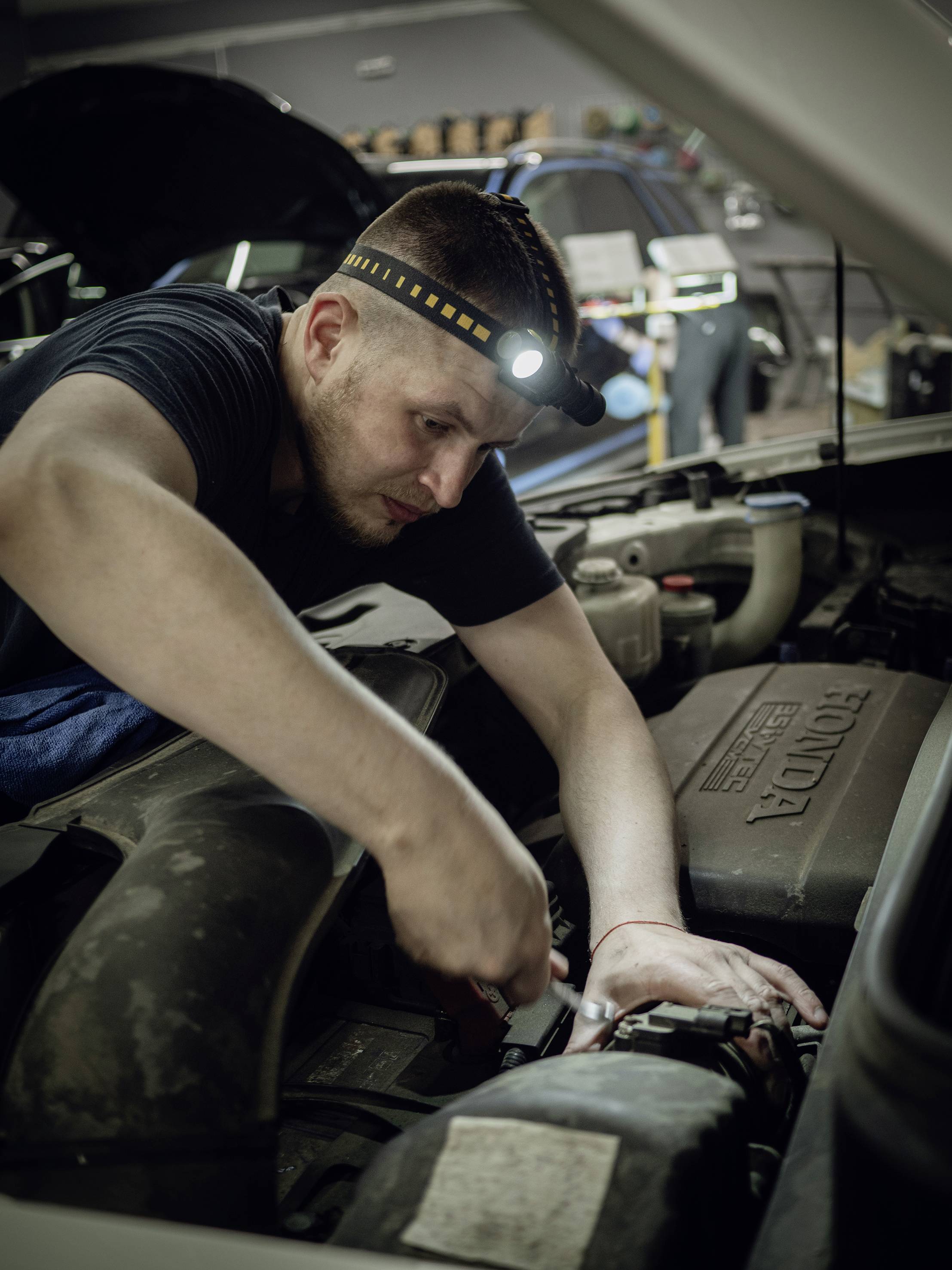 Mechanik opravuje motor v autoservise. Má na hlave čelovku, aby osvetlil priestor motora.