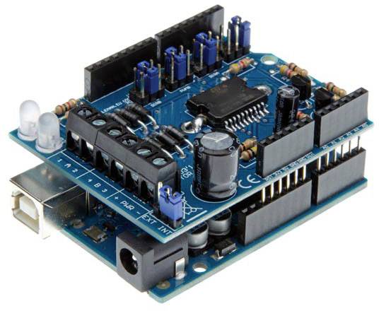 Arduino shield s viacerými pinmi, konektormi a mikrokontrolerom na modrej doske, určený na rozšírenie Arduino boardu.