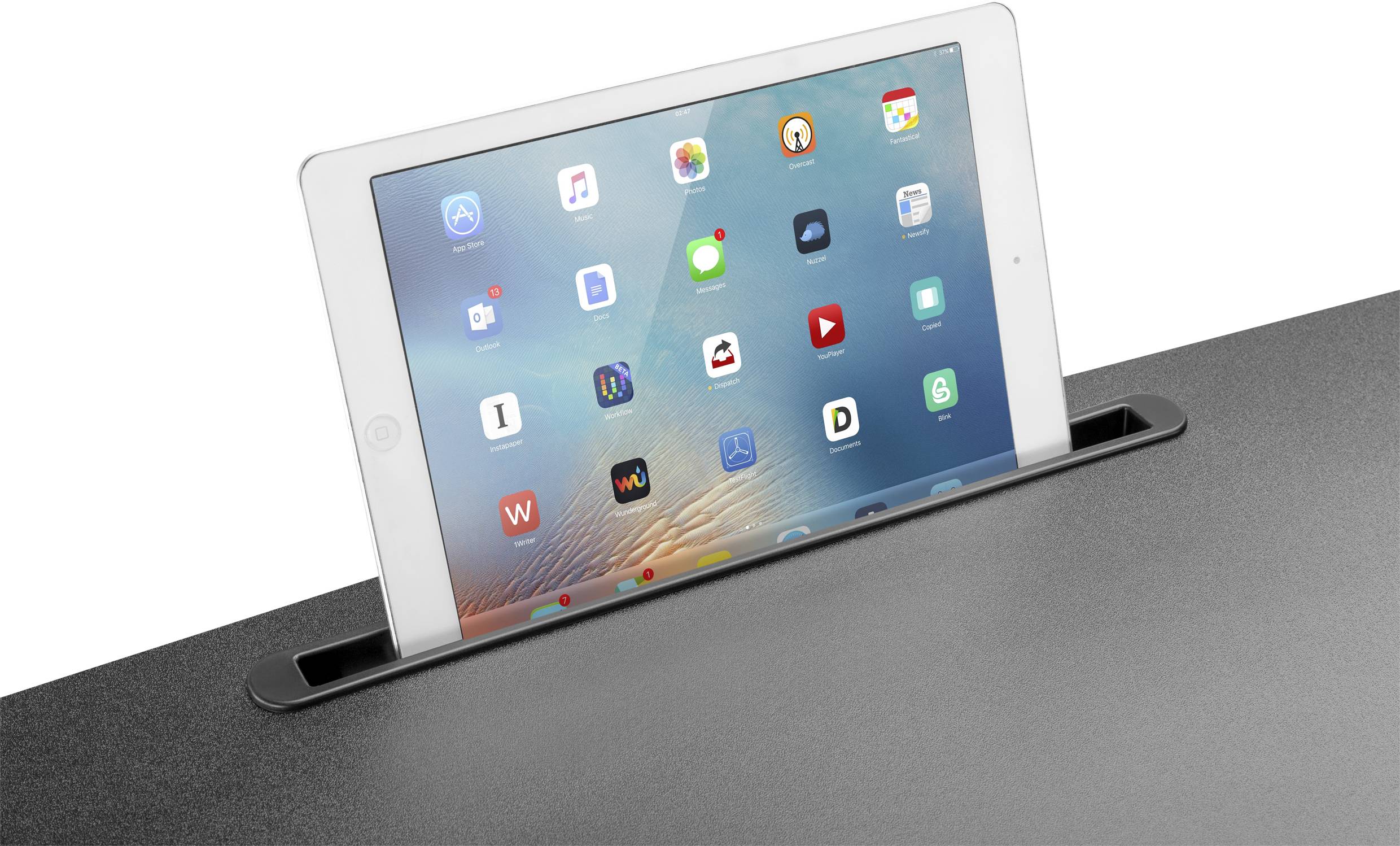 Tablet je umiestnené v držiaku. Na displeji sa zobrazuje rad ikon aplikácií na modrom pozadí.