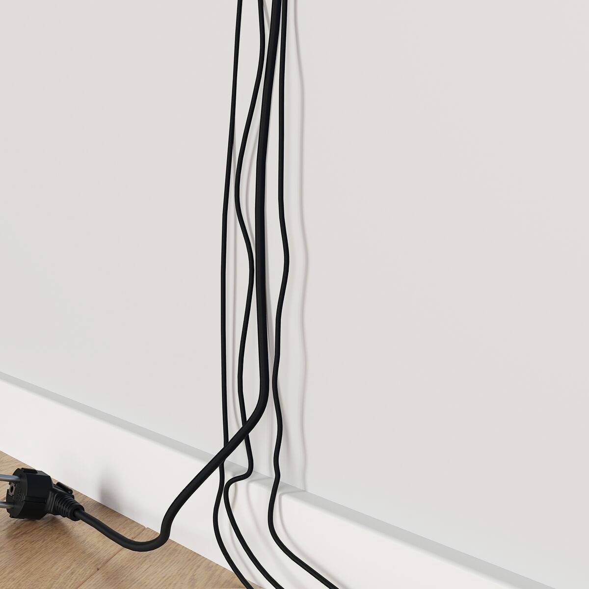 Čierne káble visia na bielej stene a voľne končia na drevenej podlahe. Zástrčka leží na podlahe.