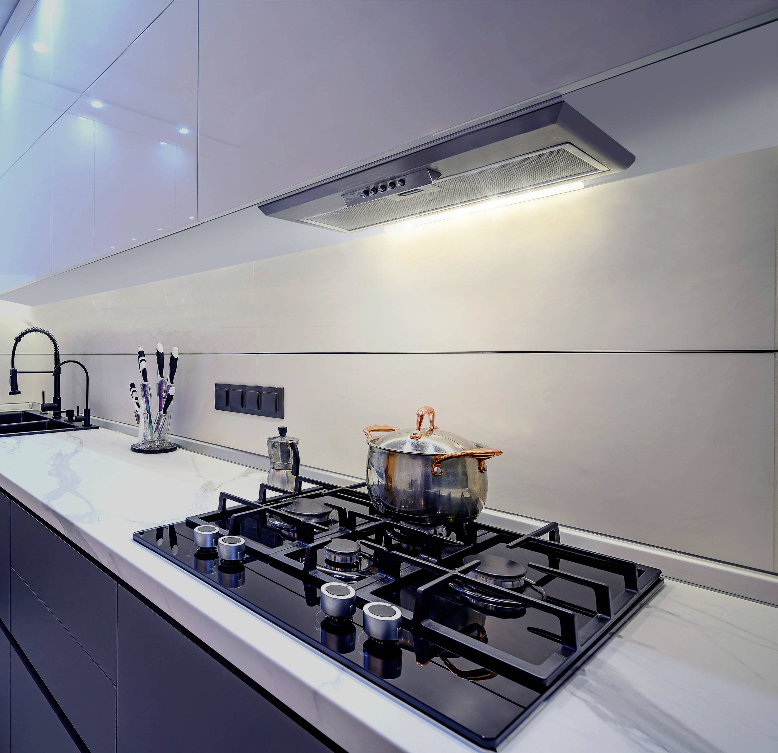 Moderná kuchyňa so sklokeramickou varnou doskou, lesklou bielou linkou a digestorom. Hrniec s pokrievkou stojí na sporáku. Minimalistický dizajn.