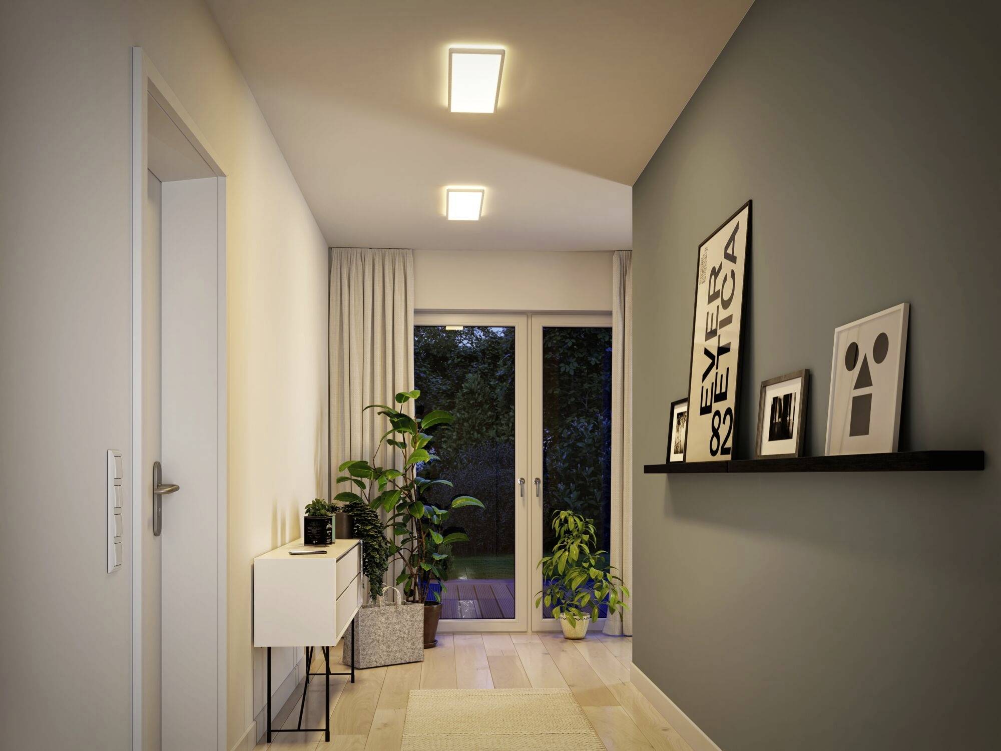 Chodba s drevenou podlahou, osvetlená stropnými svietidlami, rastliny vedľa sklenenej brány a obrázky na polici na stene.