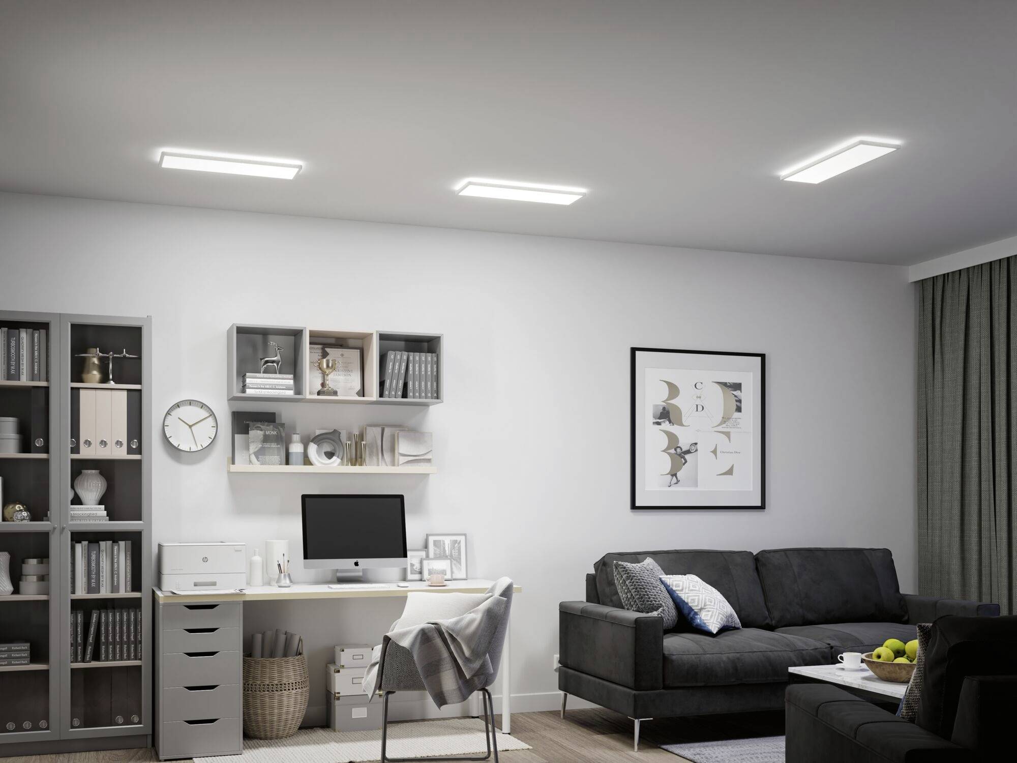 Moderne zariadená obývacia izba s pracovným priestorom, ktorá obsahuje pohovku, písací stôl, počítač, police a knihy. Priestor je jasne osvetlený troma stropnými svietidlami.