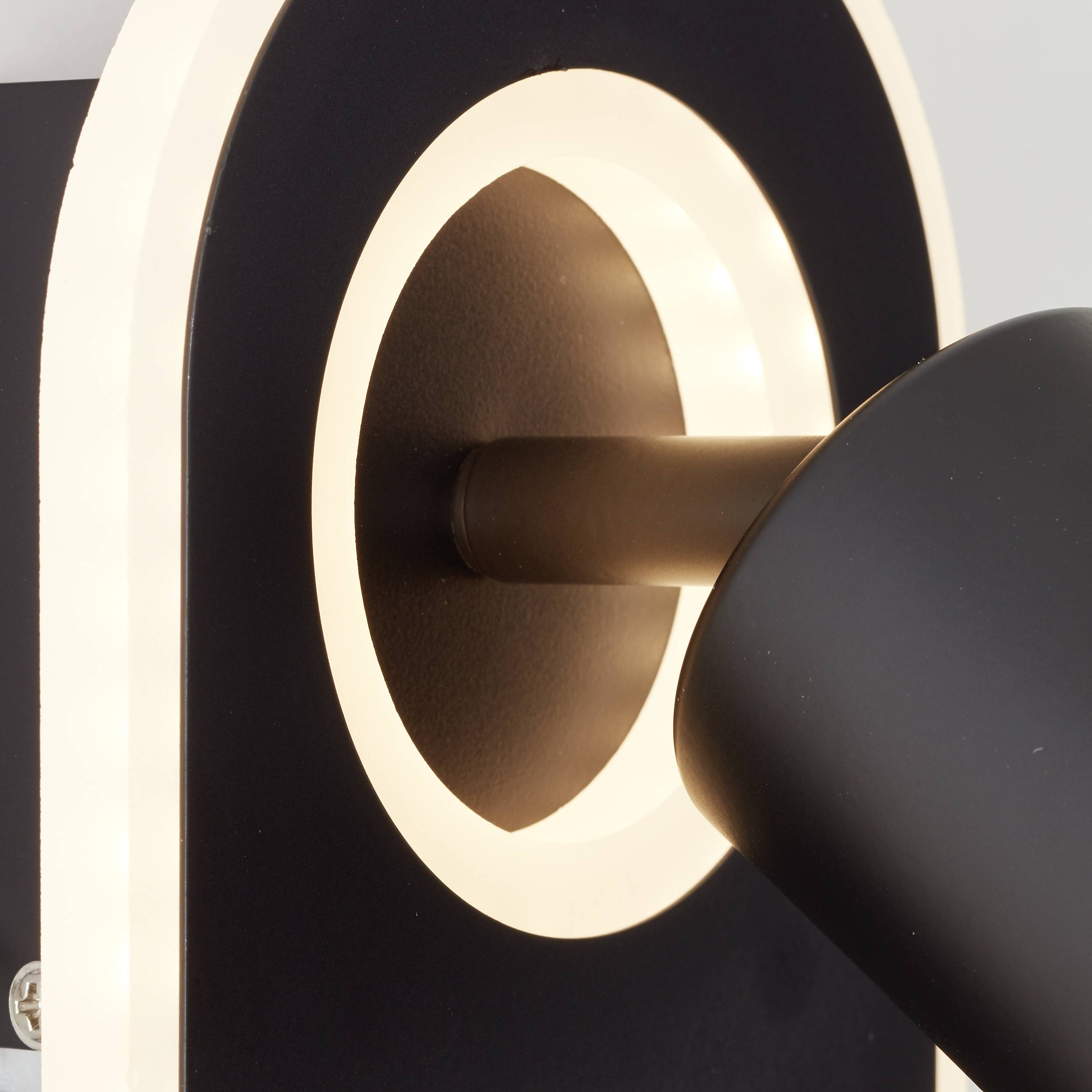 Moderná, čierna nástenná lampa s kruhovým, svietiacim okrajom, ktorá vyžaruje jemné, teplé svetlo.
