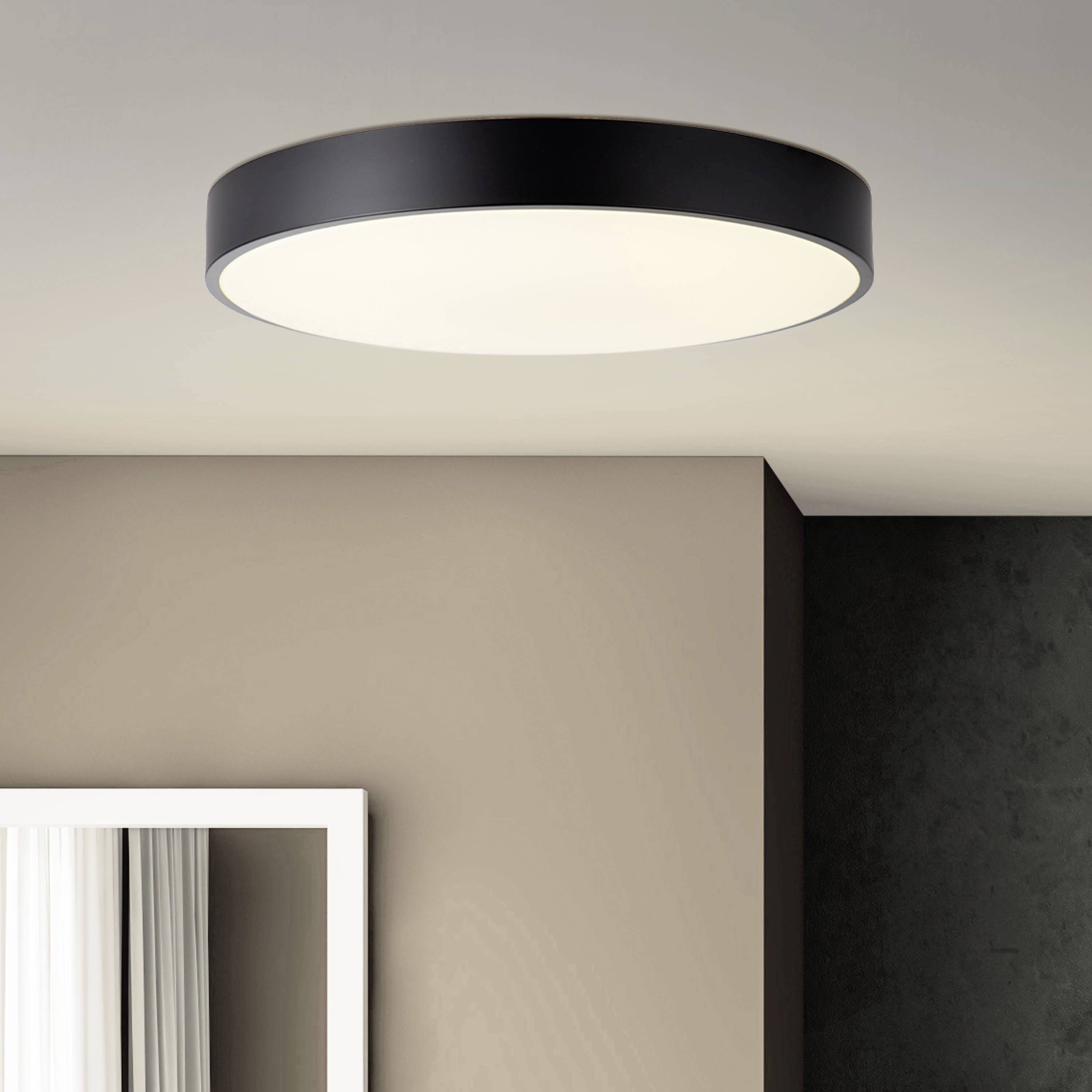 Moderná stropná lampa s čiernym lemom vyžaruje mäkké svetlo a osvetľuje miestnosť s béžovou stenou a bielym okenným rámom.